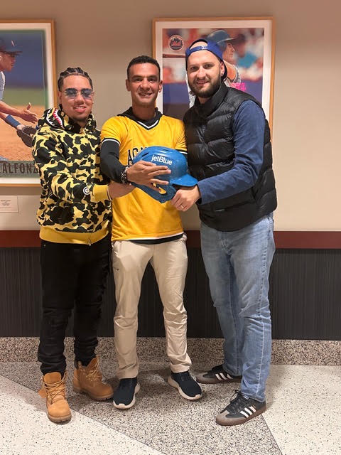An artist, a player, and a partner holding a JetBlue-branded batting helmet.